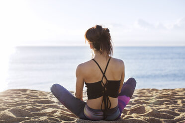 Rear view of woman doing yoga on shore at beach - CAVF33859