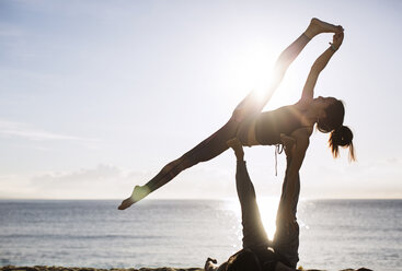 Mann hebt Frau bei der Durchführung von Yoga am Strand gegen den Himmel - CAVF33864