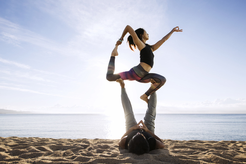 Couple doing yoga on beach against sky stock photo