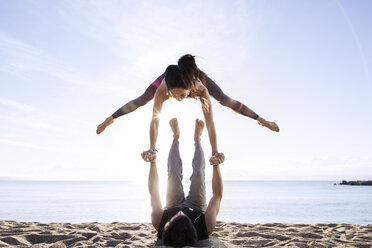 Man lifting woman while doing yoga on beach during summer - CAVF33870