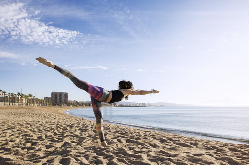 Entschlossene Frau, die am Strand Yoga in der Haltung des Kriegers 3 praktiziert - CAVF33872