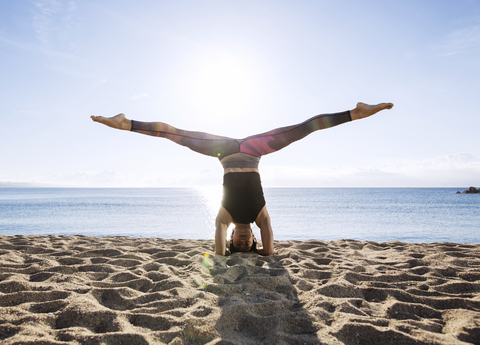 Junge Frau mit gespreizten Beinen beim Kopfstand am Strand, lizenzfreies Stockfoto