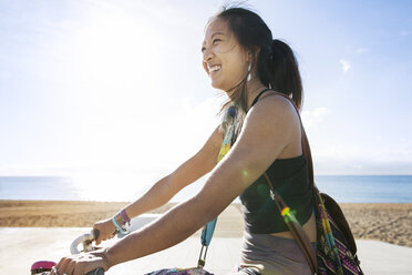 Seitenansicht einer glücklichen sportlichen Frau beim Fahrradfahren am Strand - CAVF33879