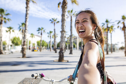Porträt einer fröhlichen Frau, die im Sommer auf der Straße Fahrrad fährt - CAVF33880