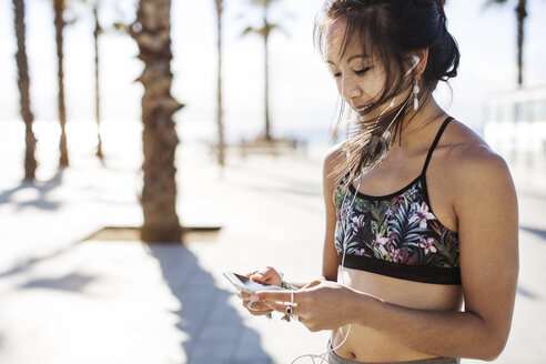 Sportliche Frau, die im Sommer auf einem Fußweg Musik über ihr Smartphone hört - CAVF33883