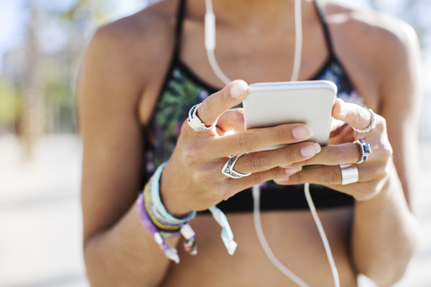 Mittelteil einer sportlichen Frau, die im Sommer ein Smartphone benutzt, lizenzfreies Stockfoto