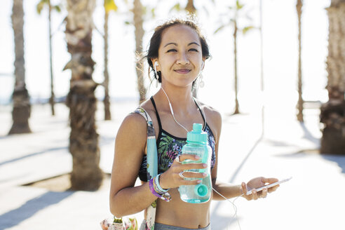 Porträt einer fröhlichen, sportlichen Frau mit Wasserflasche auf einem Fußweg im Sommer - CAVF33887