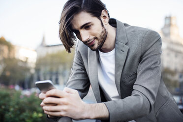 Niedriger Blickwinkel eines Geschäftsmannes, der ein Mobiltelefon benutzt und sich auf ein Geländer stützt - CAVF33907