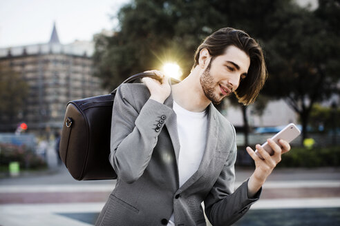 Geschäftsmann trägt Tasche und benutzt Mobiltelefon - CAVF33909