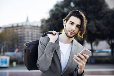 Porträt eines Geschäftsmannes, der eine Tasche trägt und ein Mobiltelefon benutzt - CAVF33910