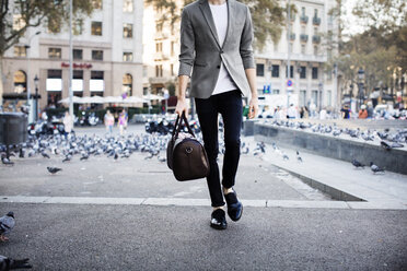 Niedriger Ausschnitt eines Mannes, der eine Tasche hält, während er auf einer Straße in der Stadt geht - CAVF33915