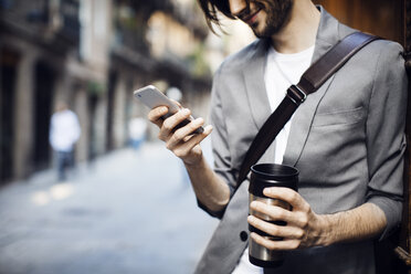 Businessman with drink using mobile phone in city - CAVF33919