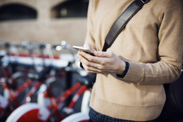 Midsection of man using mobile phone while standing at bicycle parking station - CAVF33926