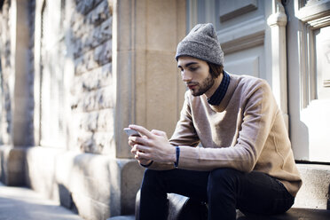 Man using mobile phone while sitting against house - CAVF33927