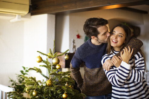 Mann küsst Freundin, während er zu Hause am Weihnachtsbaum steht - CAVF33931