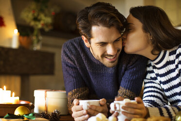 Woman kissing smiling boyfriend while having coffee at table during Christmas - CAVF33937