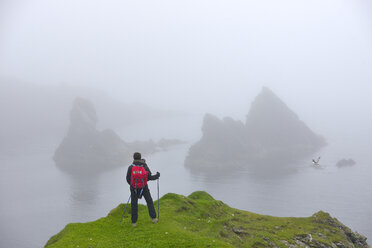 Ältere Frau schaut von einer grasbewachsenen Klippe auf den Shetland-Inseln auf einen Felsenstapel - FOLF08000