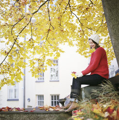Frau unter einem Ahornbaum, zwei gefallene Blätter haltend - FOLF08055