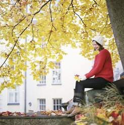 Woman under maple tree, holding two fallen leaves - FOLF08055