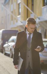 Businessman texting in sunlit street - FOLF08155