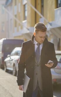 Geschäftsmann, der in einer sonnenbeschienenen Straße eine SMS schreibt - FOLF08155