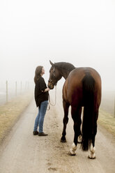 Halbwüchsige Frau mit Pferd auf unbefestigtem Weg im Nebel - FOLF08413