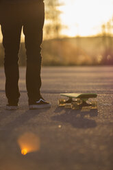 Mann mit Skateboard auf der Straße bei Sonnenuntergang - FOLF08576