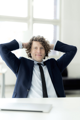 Entspannter Geschäftsmann im Büro sitzend mit den Händen hinter dem Kopf, lizenzfreies Stockfoto