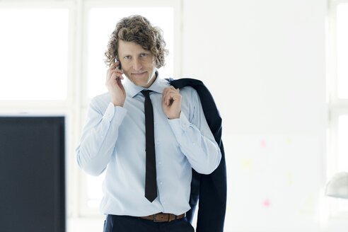 Smart businessman standing in office, using mobile phone - HHLMF00179