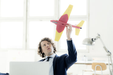 Businessman sitting in his office playing with a toy plane - HHLMF00180