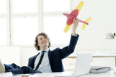 Geschäftsmann sitzt in seinem Büro und spielt mit einem Spielzeugflugzeug - HHLMF00181