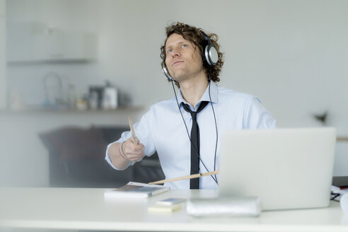 Businessman wearing headphones and drumming on his desk - HHLMF00183