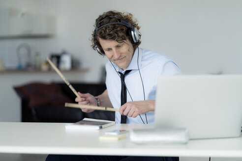 Businessman wearing headphones and drumming on his desk - HHLMF00184