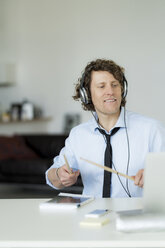 Businessman wearing headphones and drumming on his desk - HHLMF00186
