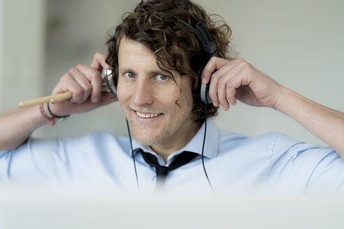 Businessman wearing headphones, holding drum sticks - HHLMF00187