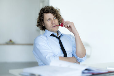 Easygoing businessman sitting in office, chewing sweets - HHLMF00193