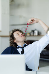 Easygoing businessman sitting in office, chewing sweets - HHLMF00195