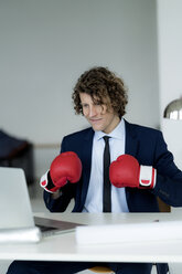 Businessman looking at laptop, wearing boxing gloves - HHLMF00206