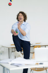 Lachender Geschäftsmann jongliert Bälle in seinem Büro - HHLMF00212