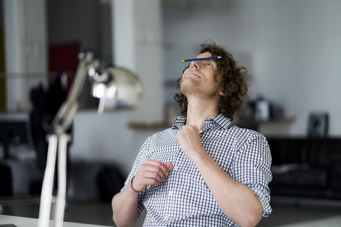 Businessman balancing pencil on his face - HHLMF00214