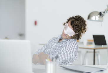 Ein überarbeiteter Geschäftsmann schläft mit einer Schlafmaske an seinem Schreibtisch - HHLMF00219