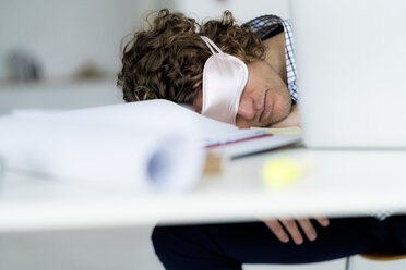 Ein überarbeiteter Geschäftsmann schläft mit einer Schlafmaske an seinem Schreibtisch - HHLMF00220