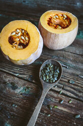 Two halves of a pumpkin and spoon of pumpkin seed on wood - GIOF03892