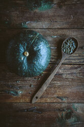 Green pumpkin and spoon of pumpkin seed on dark wood - GIOF03893