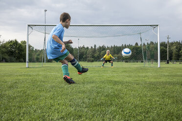 Junger Fußballspieler, der den Ball vor dem Tor mit dem Torwart kickt - WESTF24040