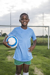 Porträt eines lächelnden jungen Fußballspielers, der einen Ball auf einem Fußballplatz hält - WESTF24041