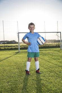 Porträt eines lächelnden jungen Fußballspielers, der einen Ball auf einem Fußballplatz hält - WESTF24046