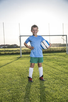 Portrait of smiling young football player holding ball on football ground - WESTF24046