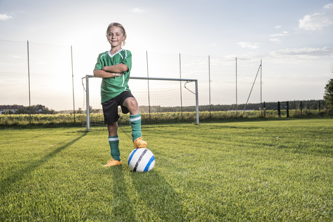 Porträt eines selbstbewussten jungen Fußballspielers mit Ball auf dem Fußballplatz, lizenzfreies Stockfoto