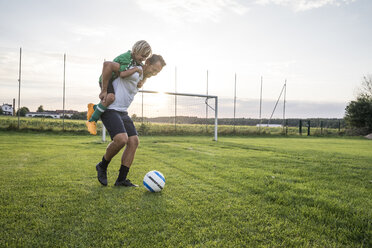 Trainer trägt jungen Fußballspieler auf dem Fußballplatz bei Sonnenuntergang - WESTF24054